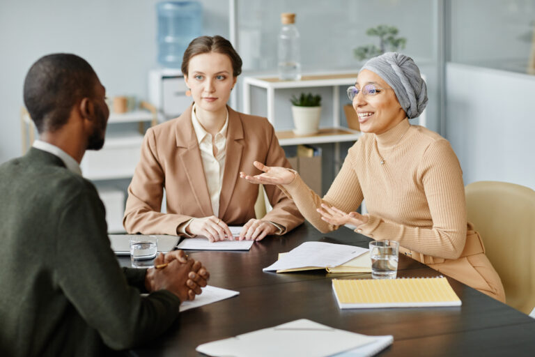 Diverse group of people in meeting or job interview at office setting, focus on Middle Eastern woman speaking and gesturing