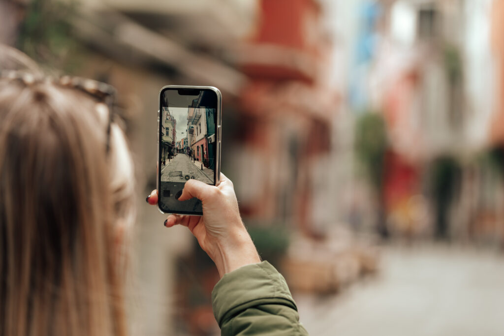 Woman tourist taking photo with phone in the street back view